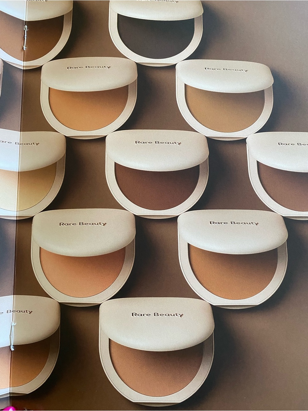 Rare Beauty pressed powder compacts in warm beige and tan tones
